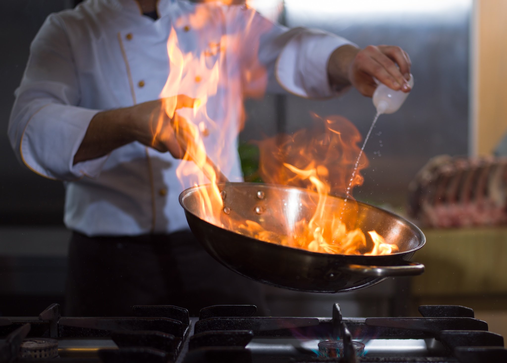 Chef cooking with flames in a pan, pouring liquid.