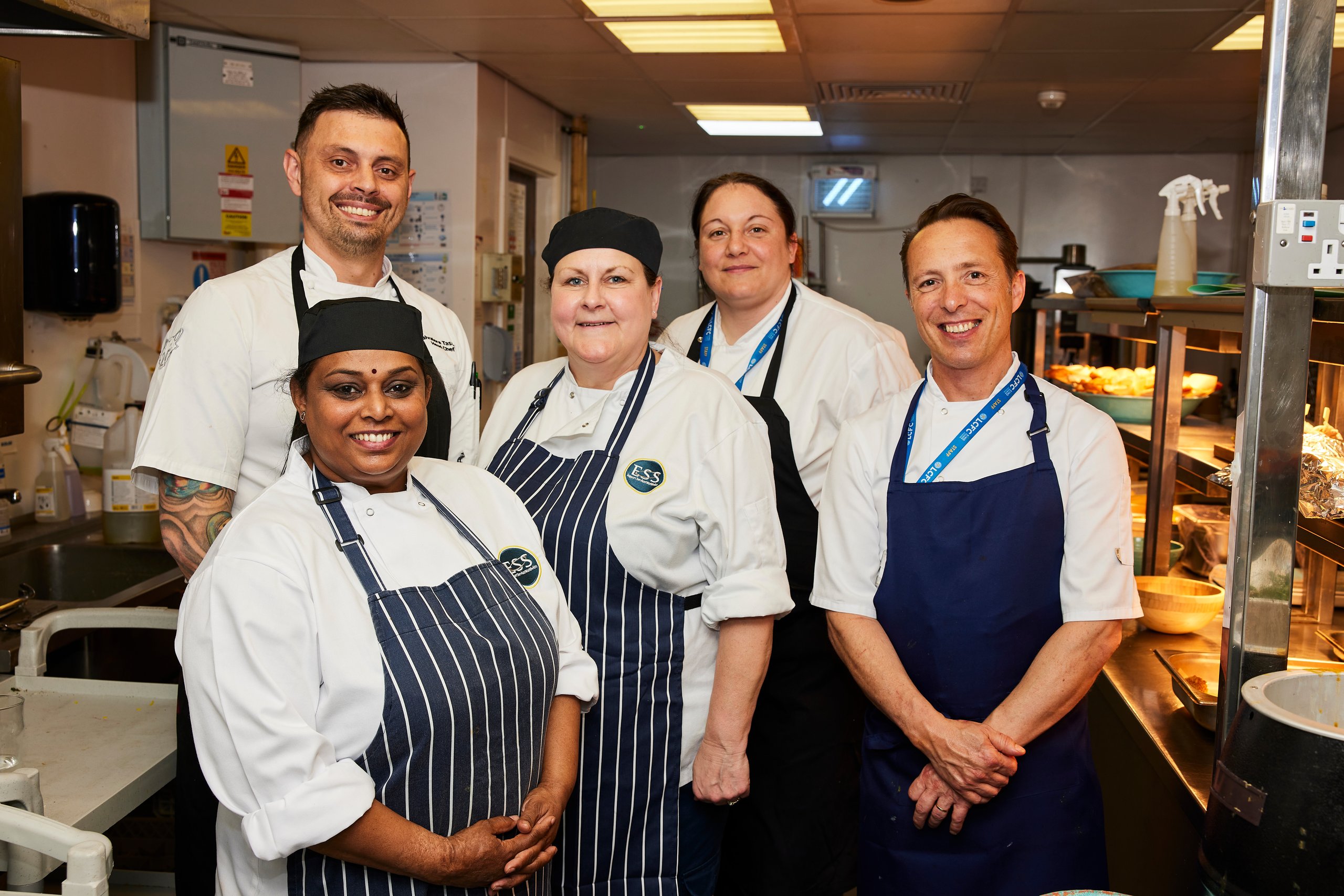 Chefs standing in a commercial kitchen smiling at the camera.