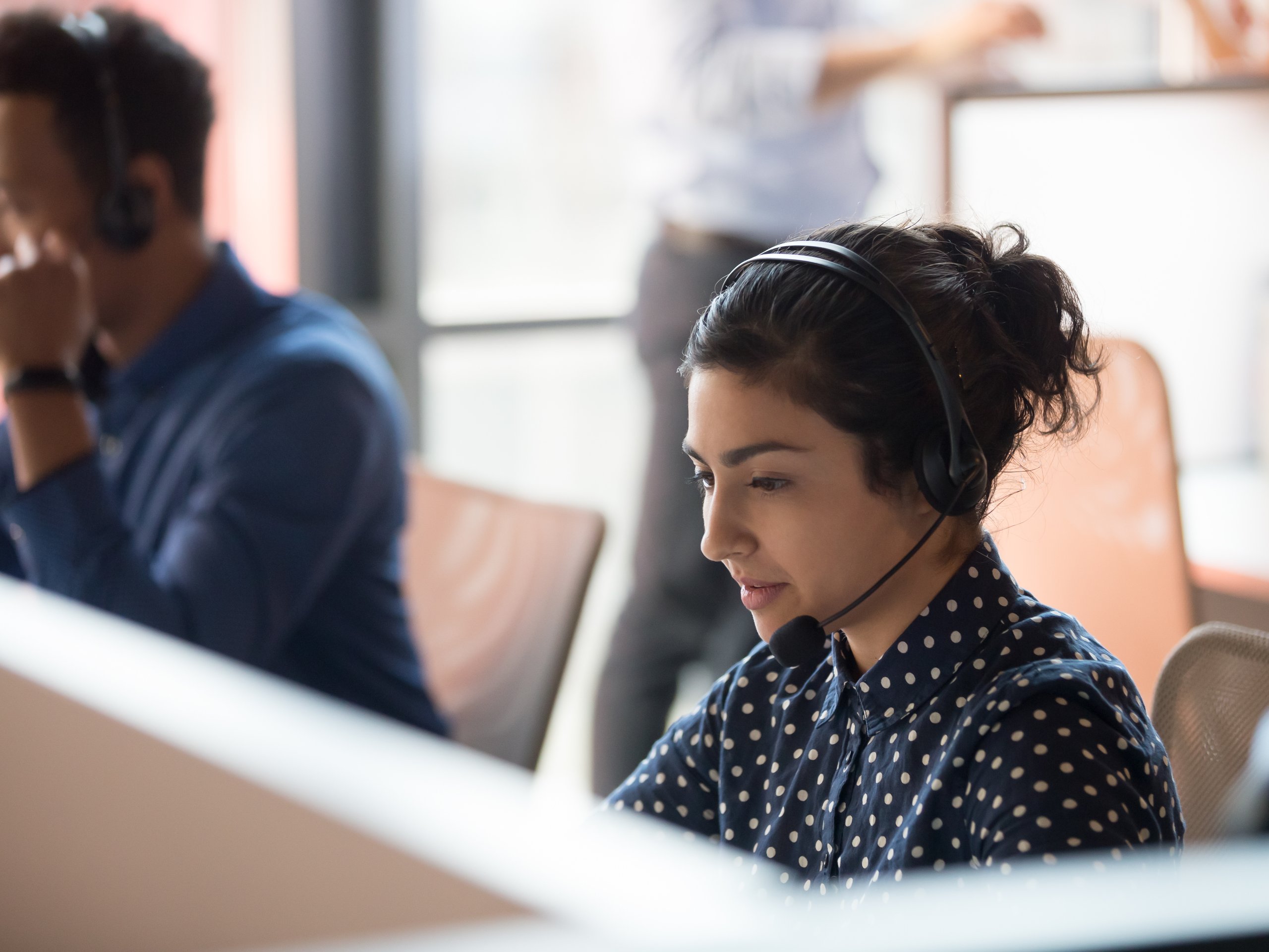 Woman with headset at a call center with coworkers in background.