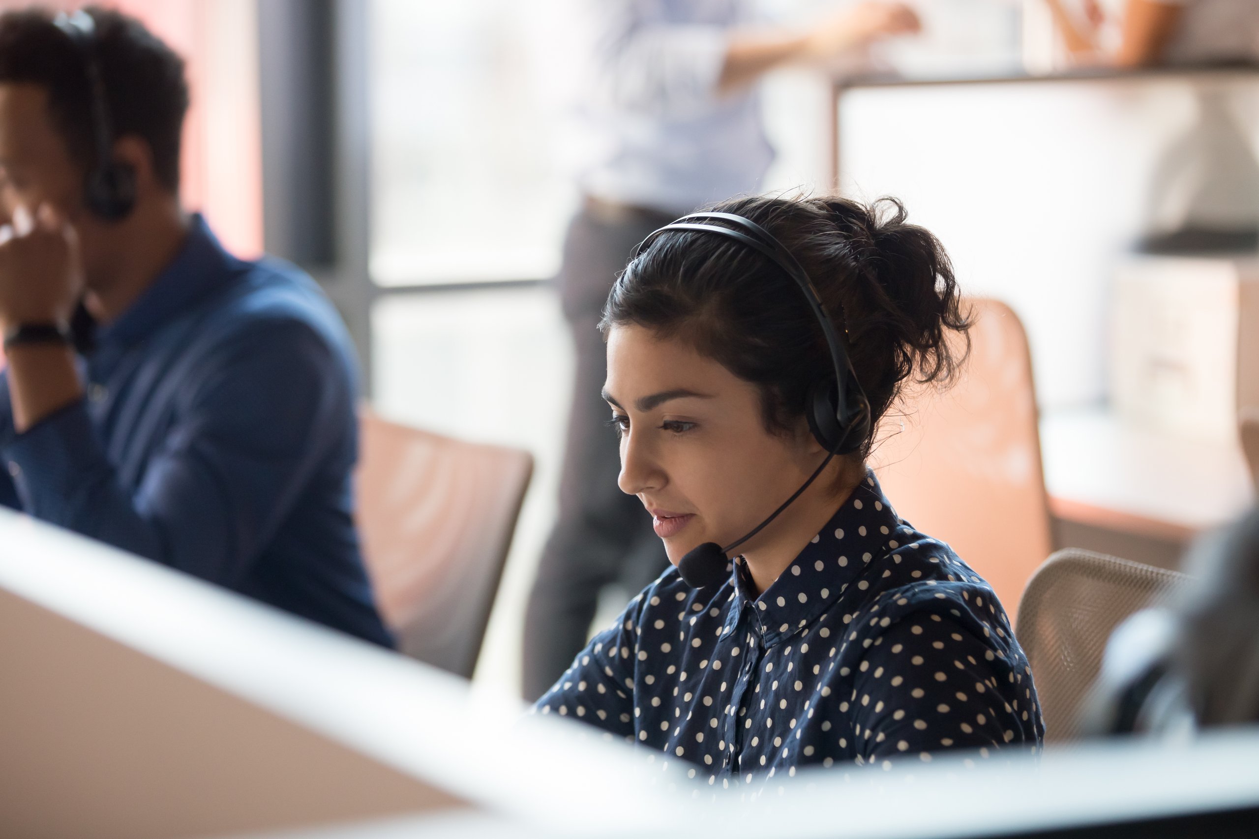 Woman with headset at a call center with coworkers in background.