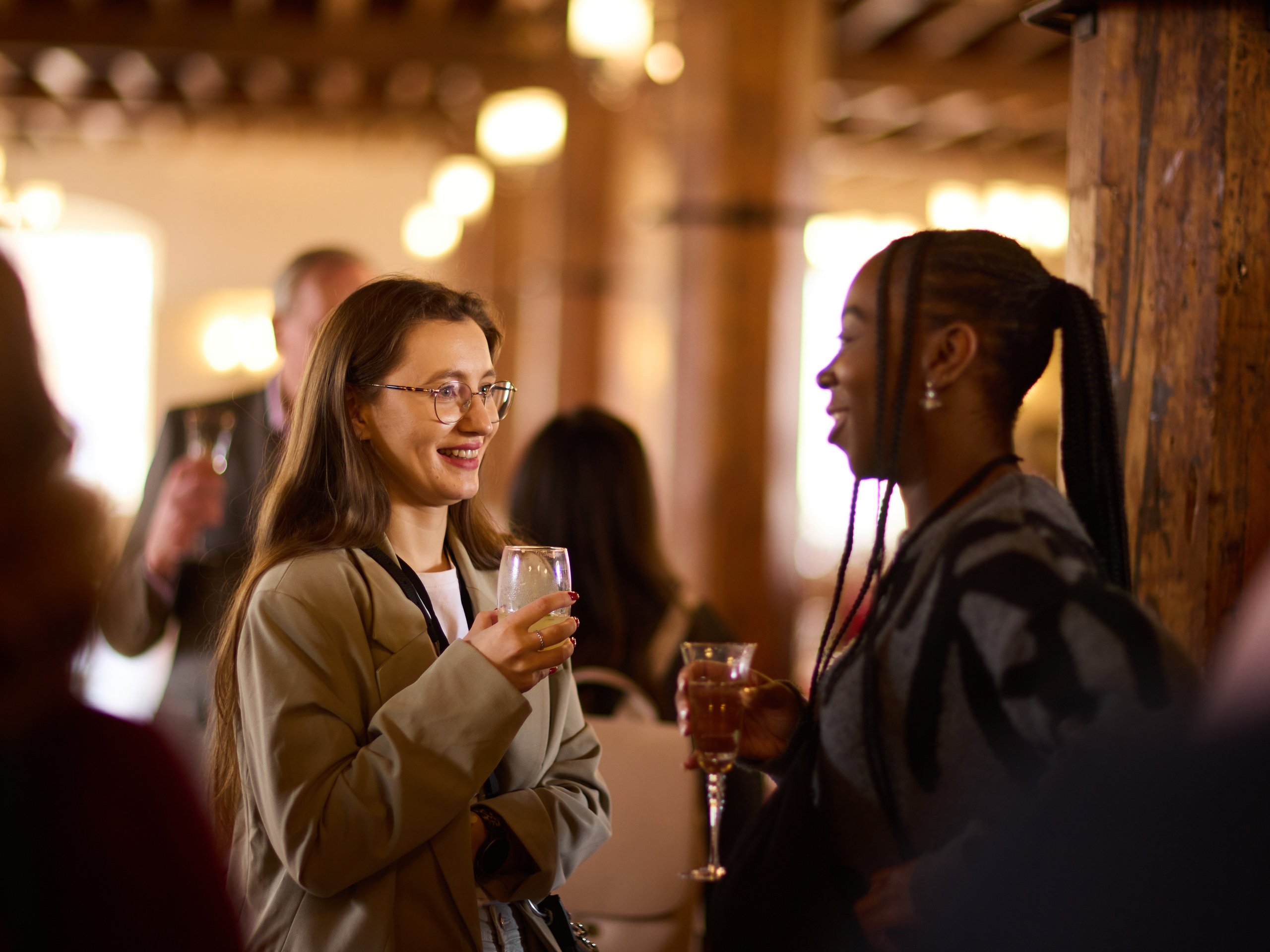 Two women in a room with drinks, talking and smiling.