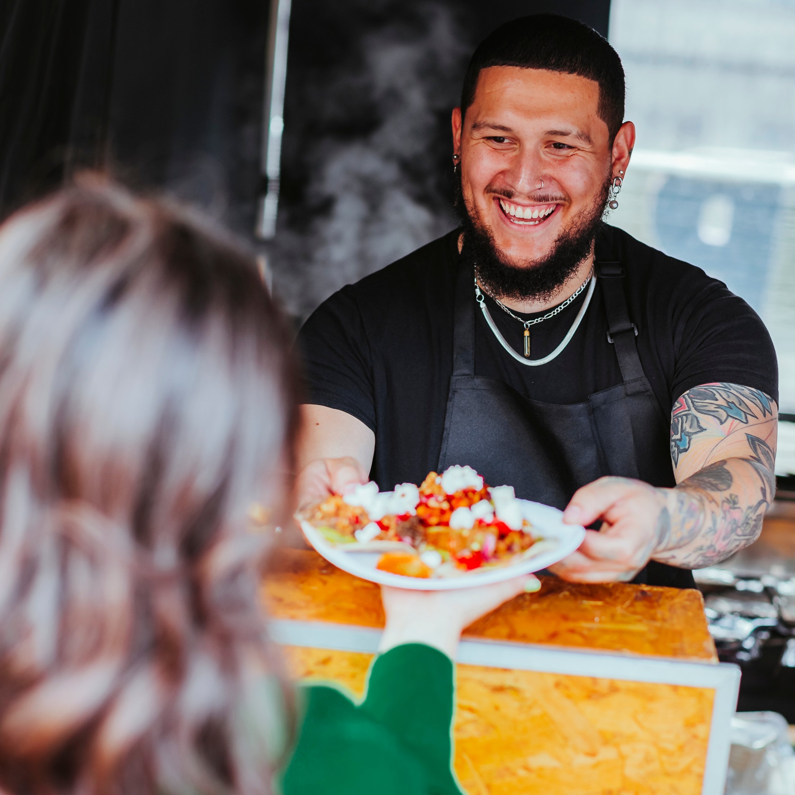 Man serving plate of food to a person. He is smiling.