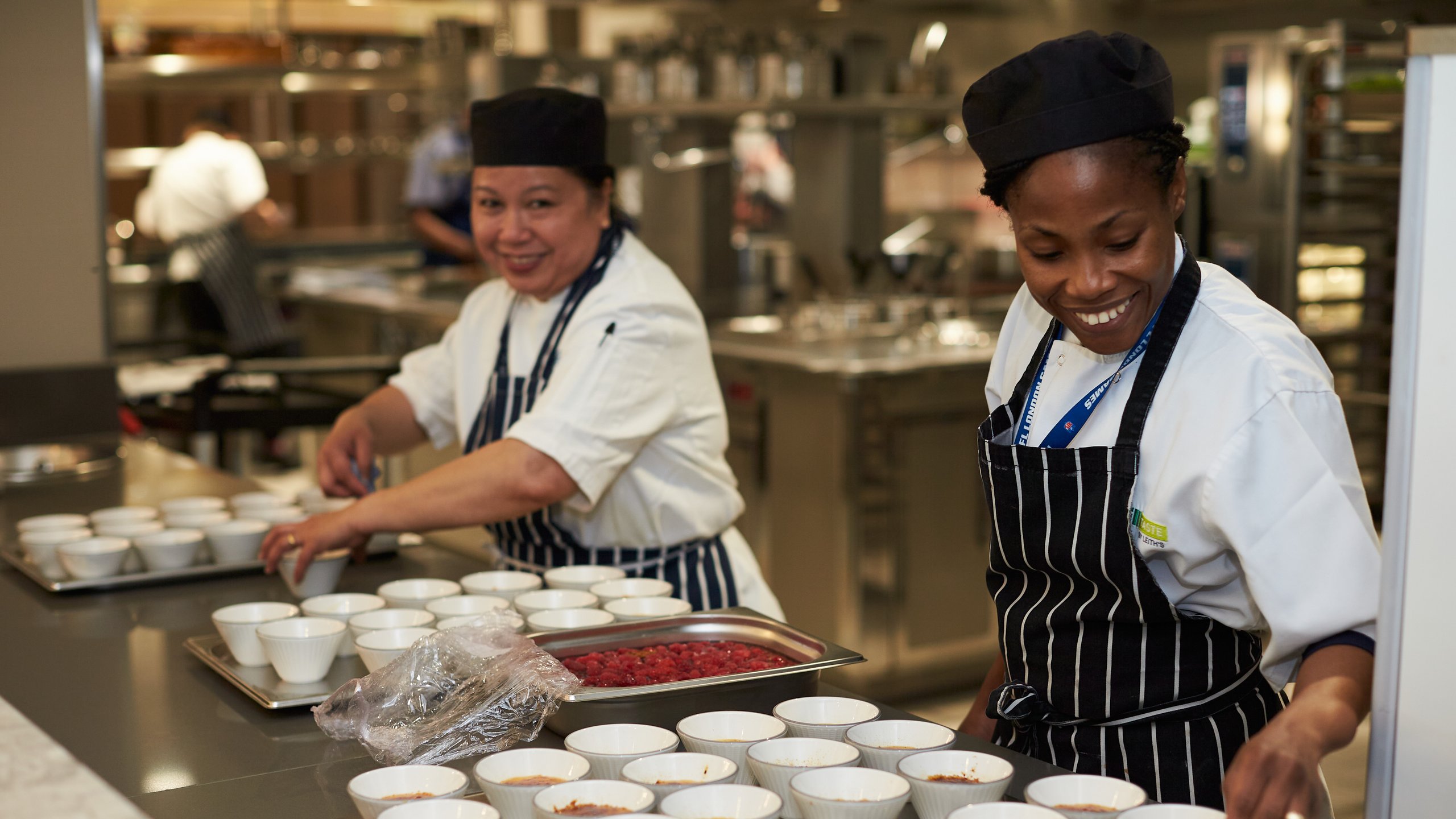 Chefs preparing food in a commercial kitchen with many bowls.