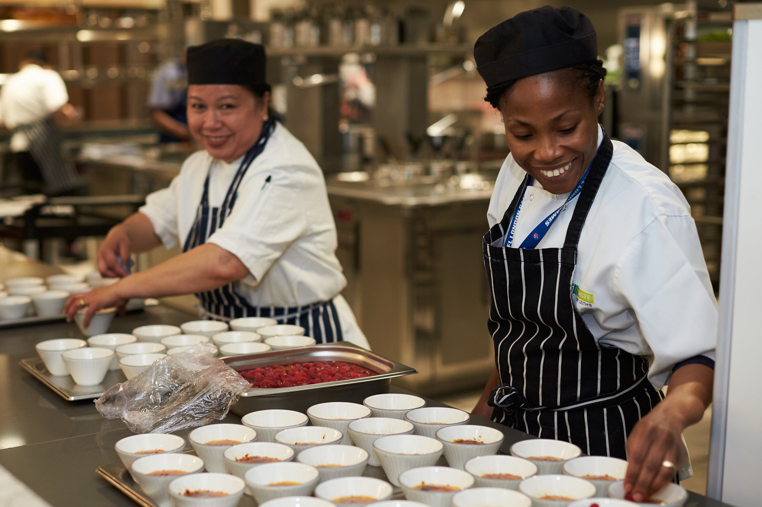 Chefs preparing food in a commercial kitchen with many bowls.