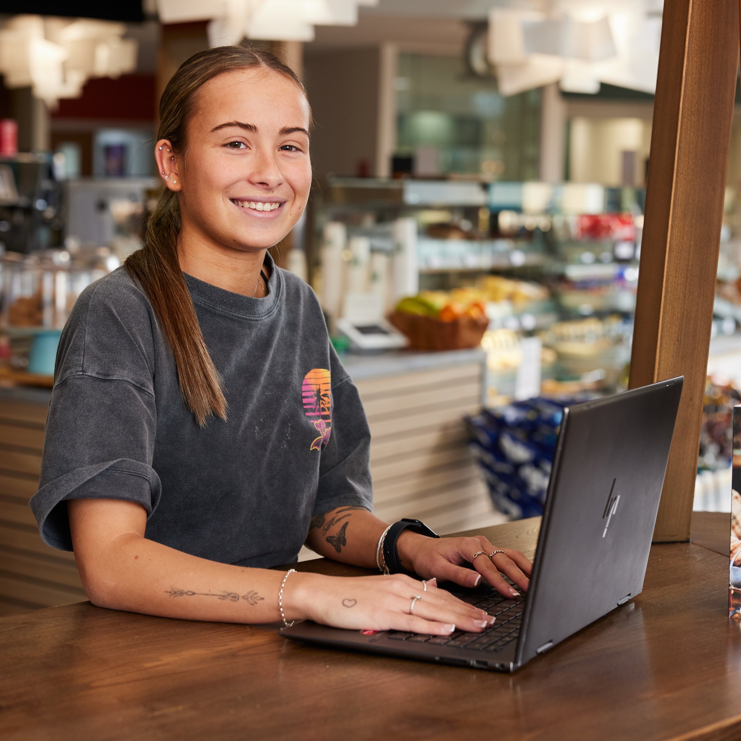 Woman smiling at a table with laptop and a "Did We Make You Smile?" sign.