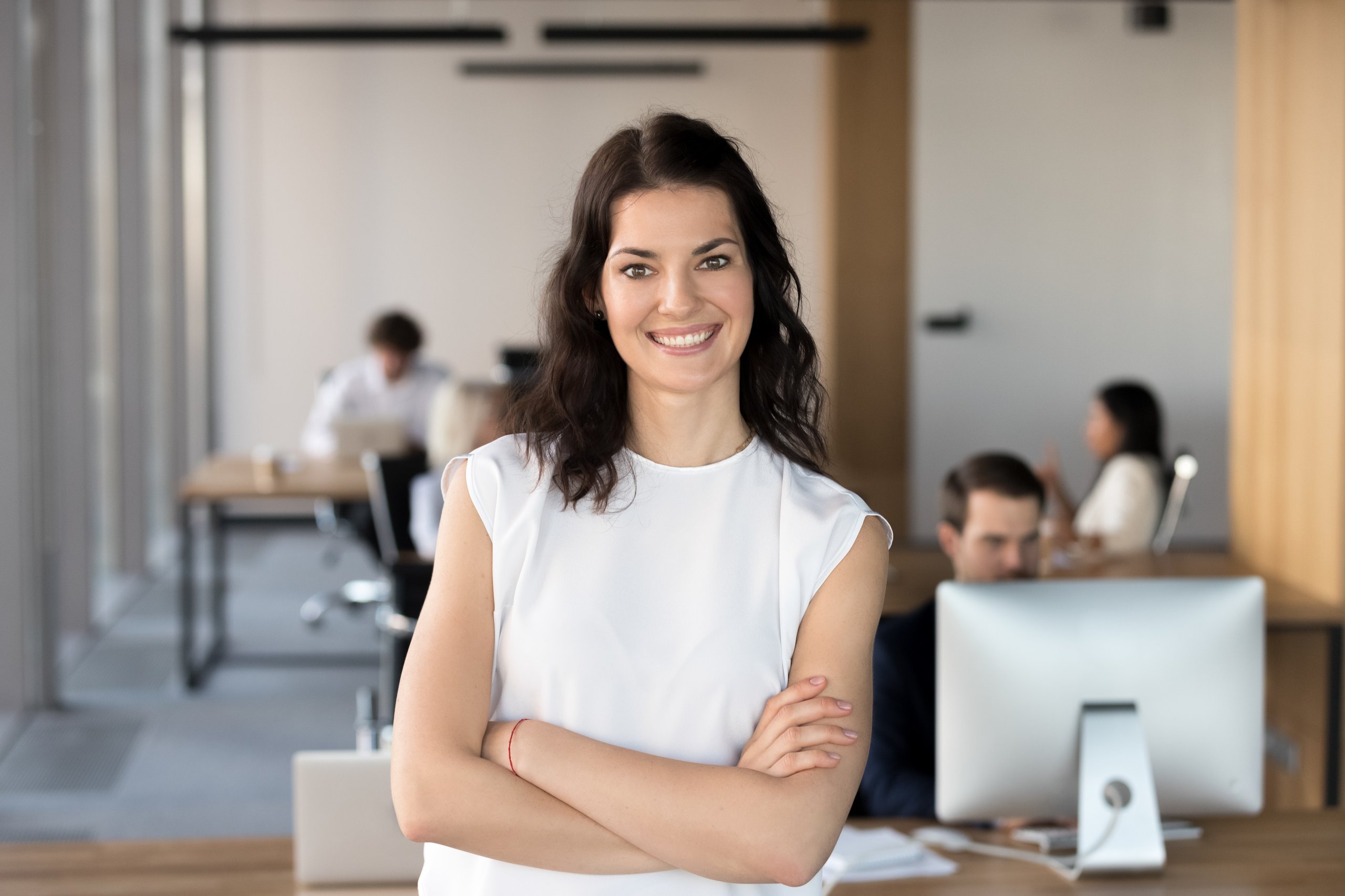 Woman smiling, arms crossed in office setting.