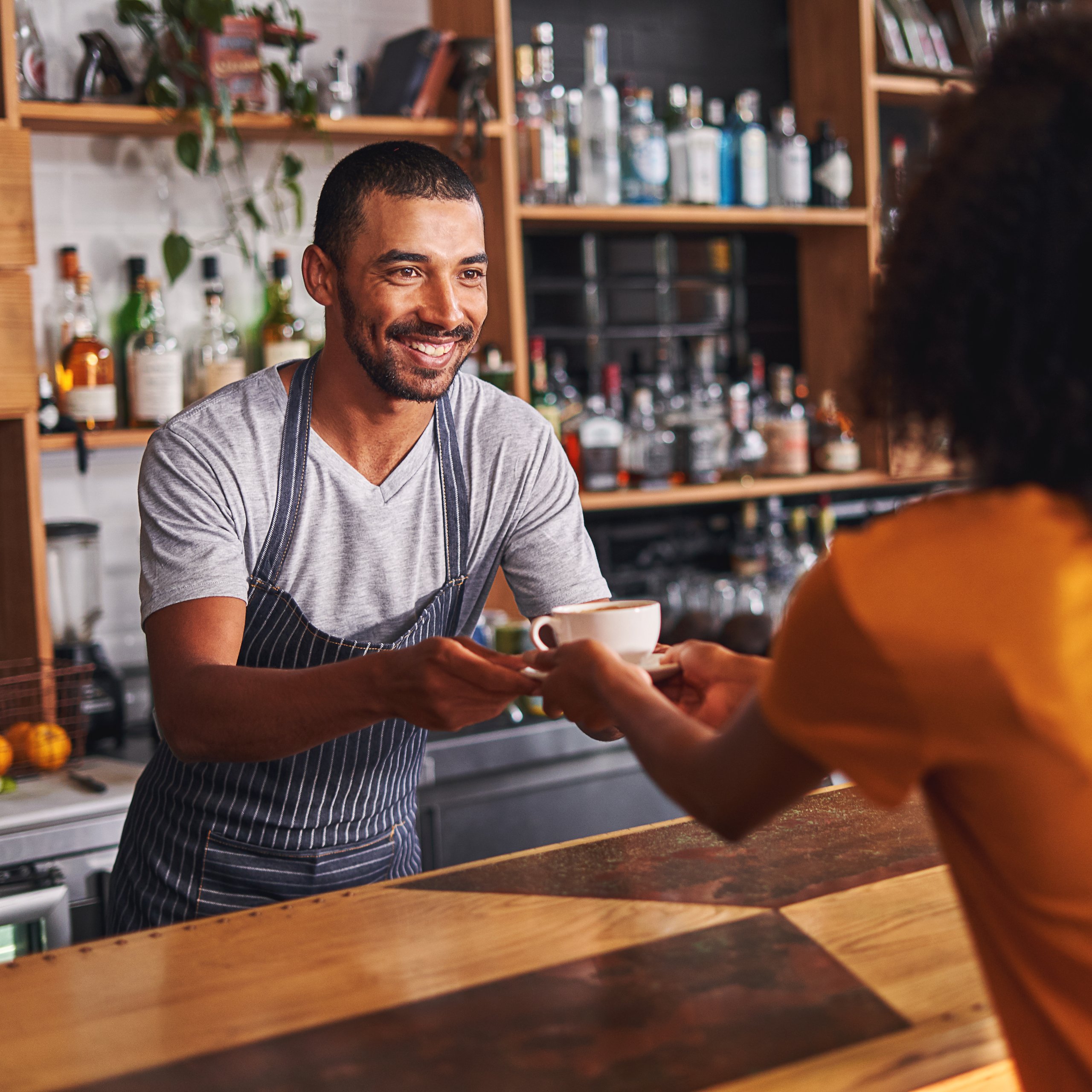 Barista hands a cup of coffee to a customer in a cafe.