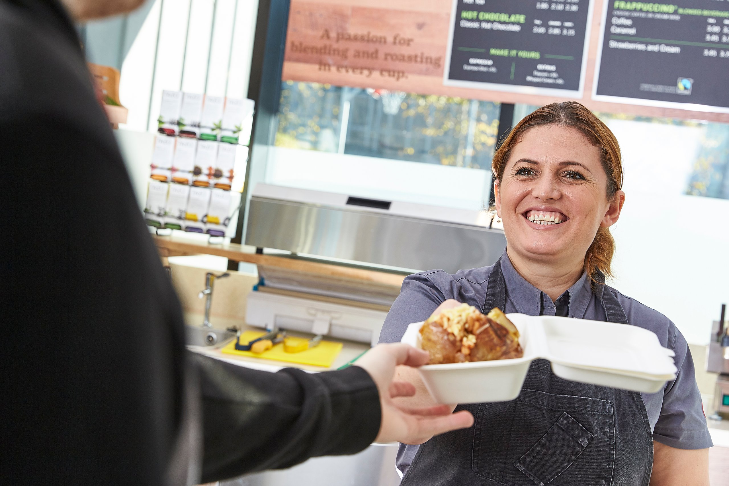 Smiling waitress hands customer baked potato in restaurant.