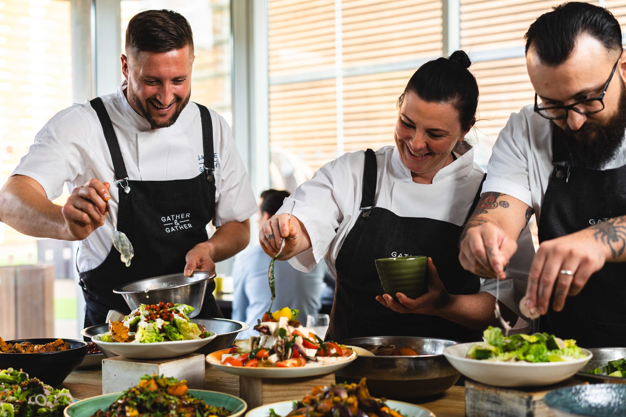 Three chefs plating salads, working in a restaurant setting.