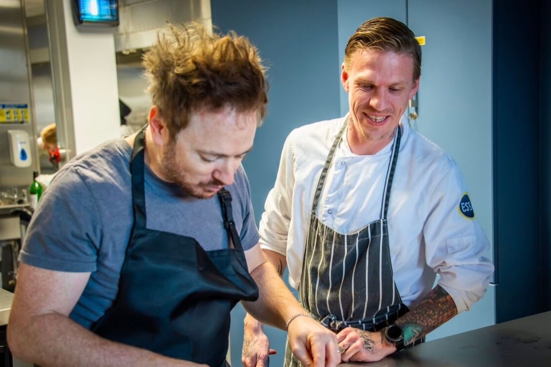 Chefs in aprons preparing a dish in a kitchen.
