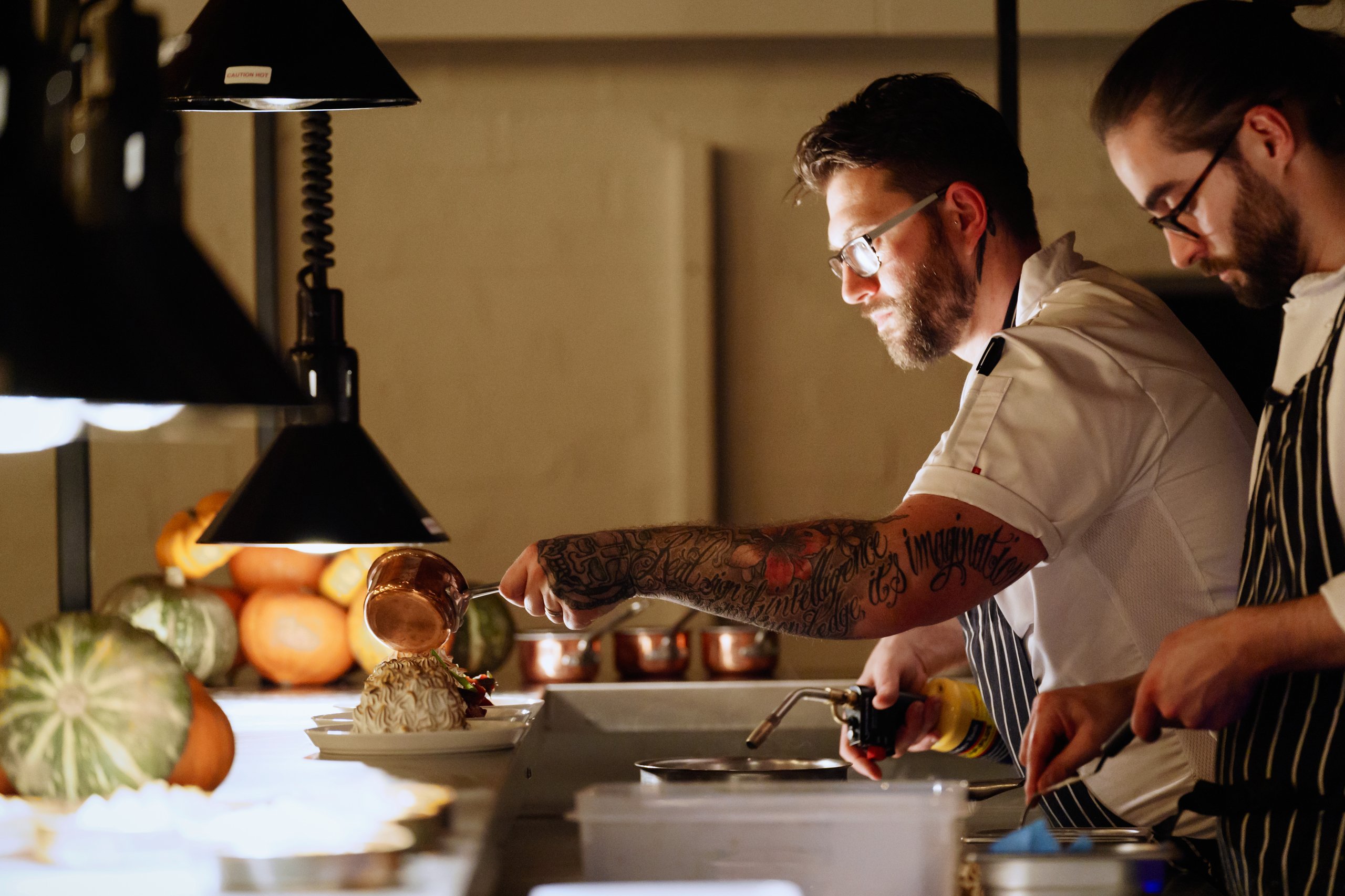 Chefs working in a kitchen with a tattooed arm.