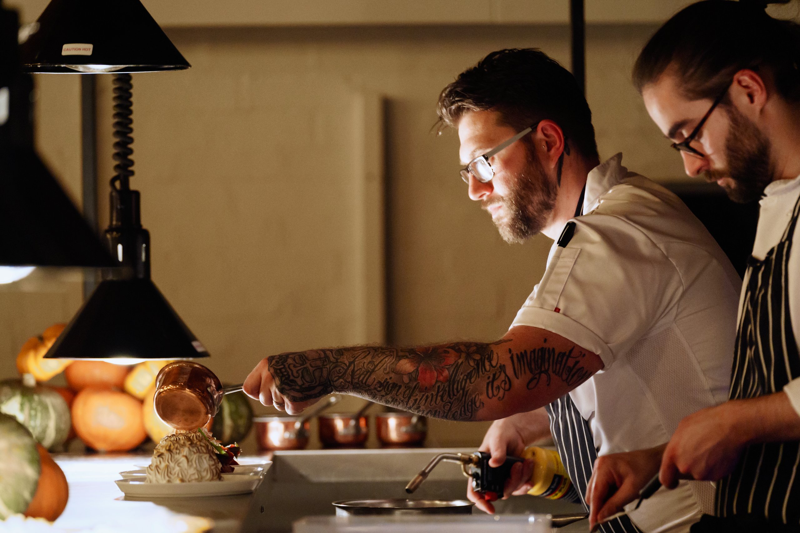 Chefs working in a kitchen with a tattooed arm.