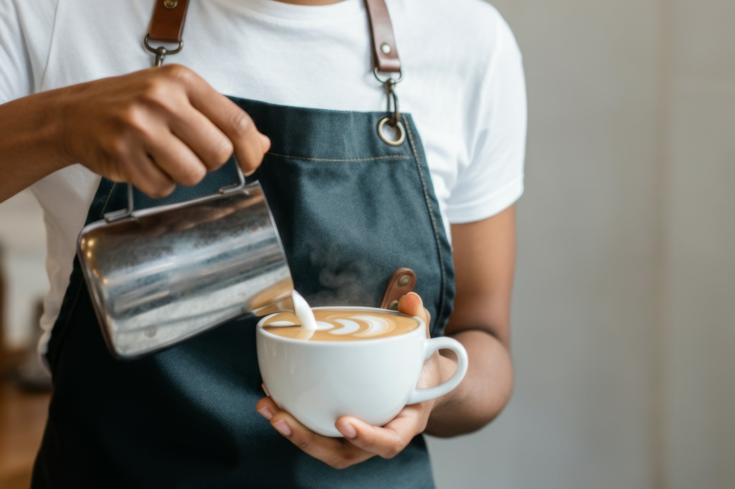 Barista pouring milk into a coffee cup, creating latte art.