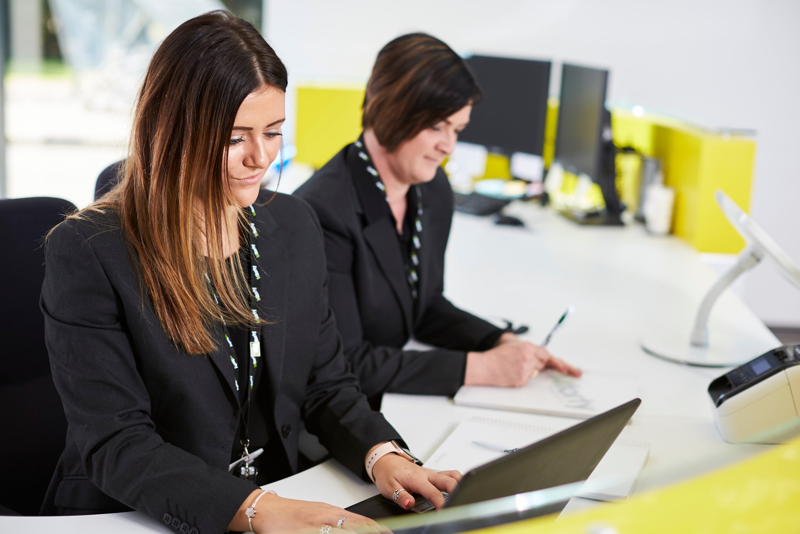 Two women working at a desk with computers.