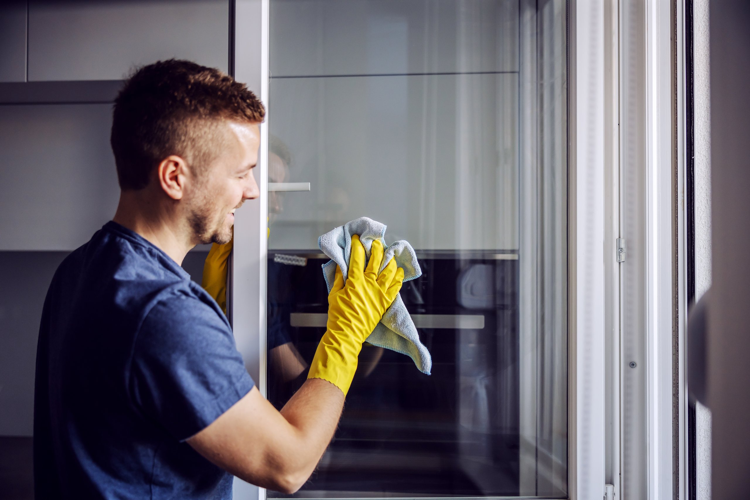 Man cleaning a window with a microfiber cloth and yellow gloves.