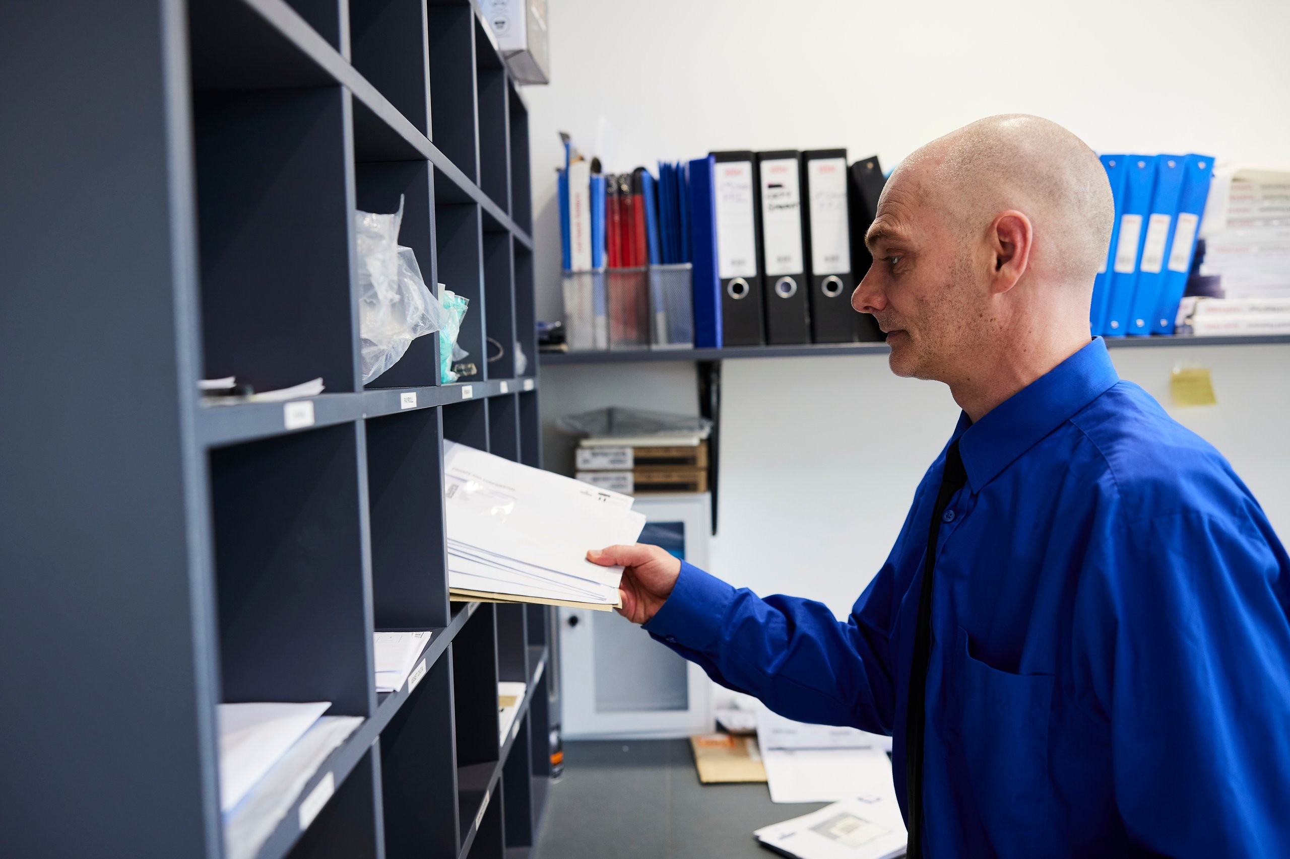 Man sorting mail in a mailroom with blue shirt.