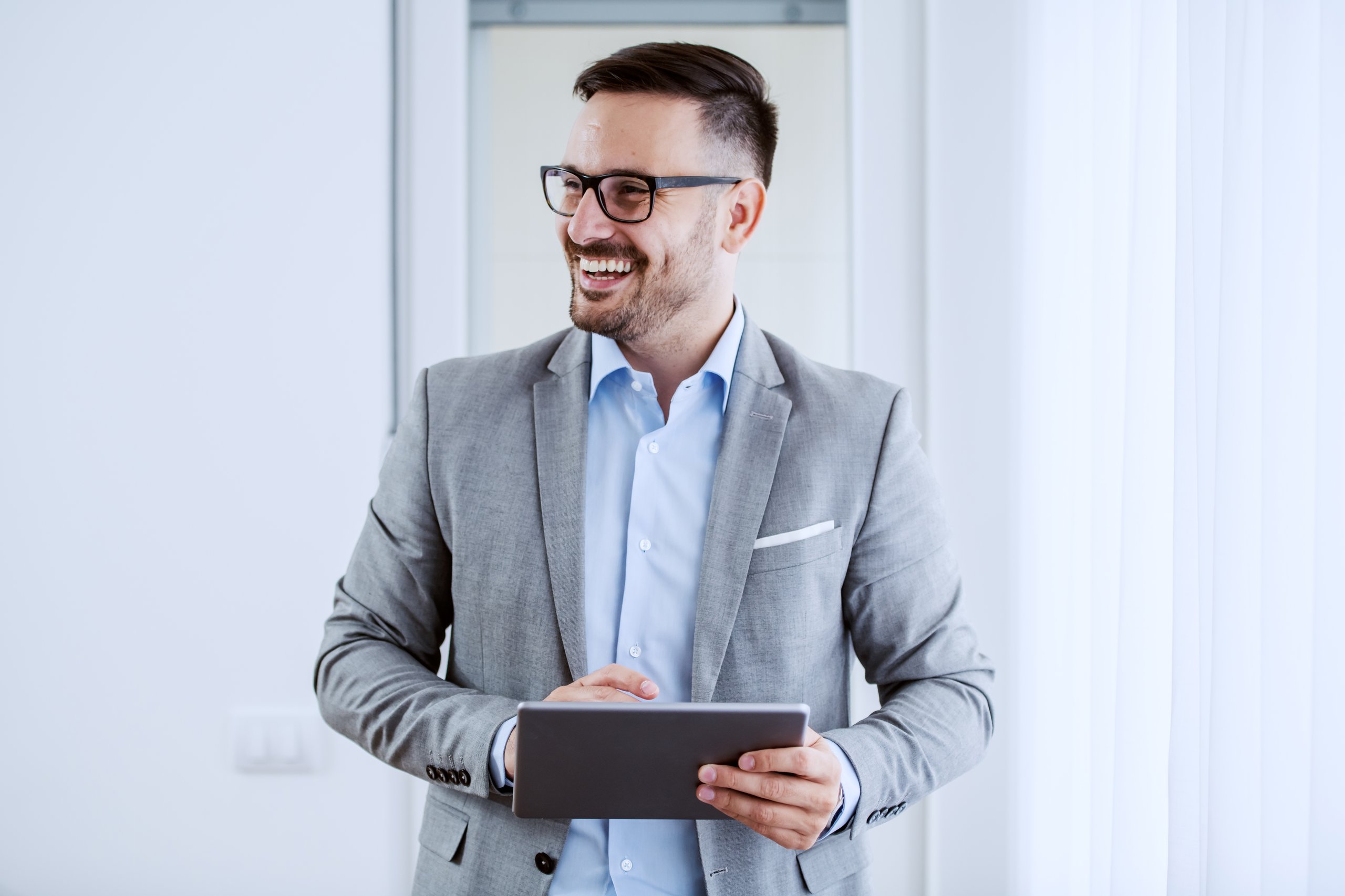 Man wearing glasses and a suit, holding a tablet.