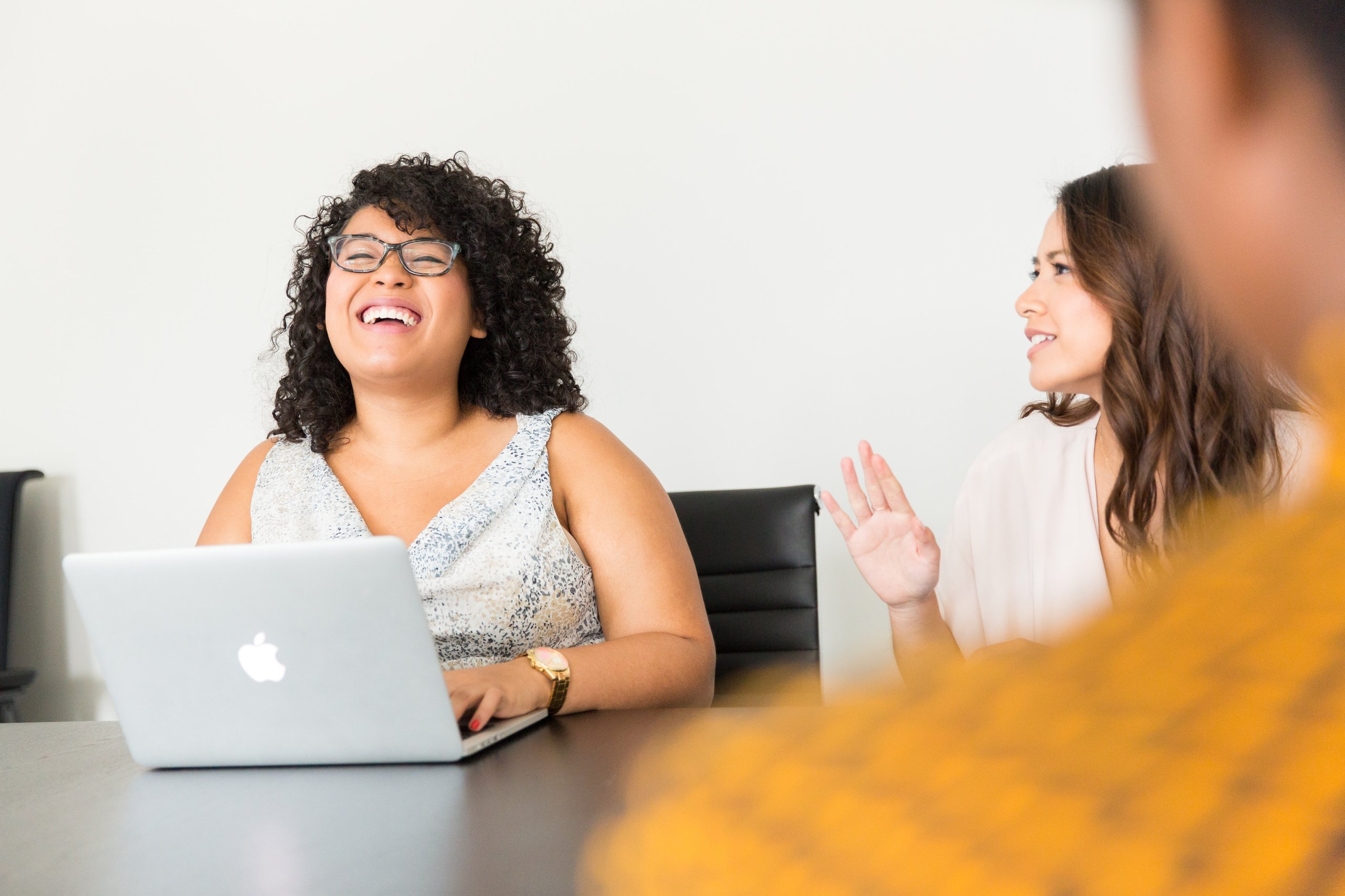 Women laughing and working on laptop at table.