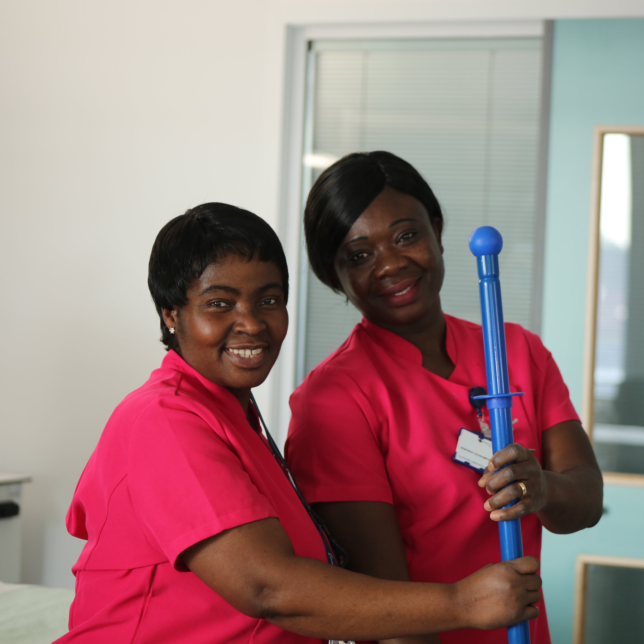 Two healthcare workers smiling, one holding a cleaning tool.