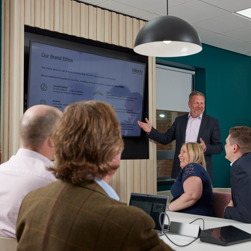 Man giving presentation to group; screen shows "Our Brand Ethos"