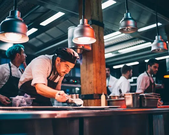 Chefs prepare food in a busy restaurant kitchen with warm lighting.