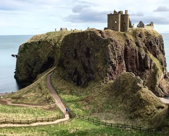 A winding path leads up to the ruins of Dunnottar Castle, perched dramatically on a cliff overlooking the sea.