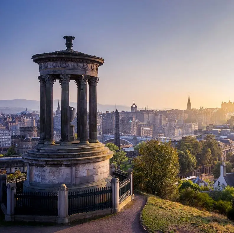 Dugald Stewart Monument overlooking Edinburgh cityscape at sunrise, with Calton Hill and city skyline in the background.