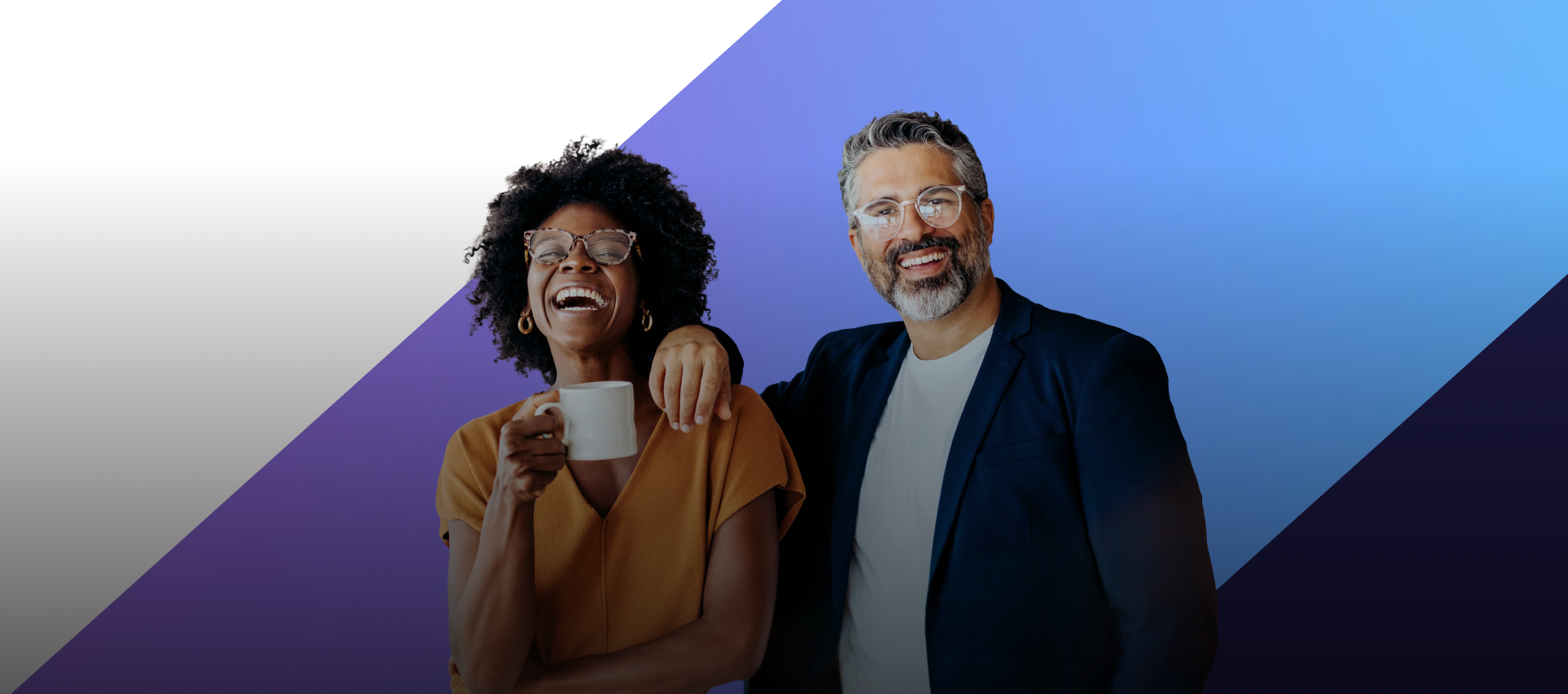 Two colleagues, a Black woman with glasses holding a mug and laughing, and a white man with glasses and a beard, stand together with his arm around her.