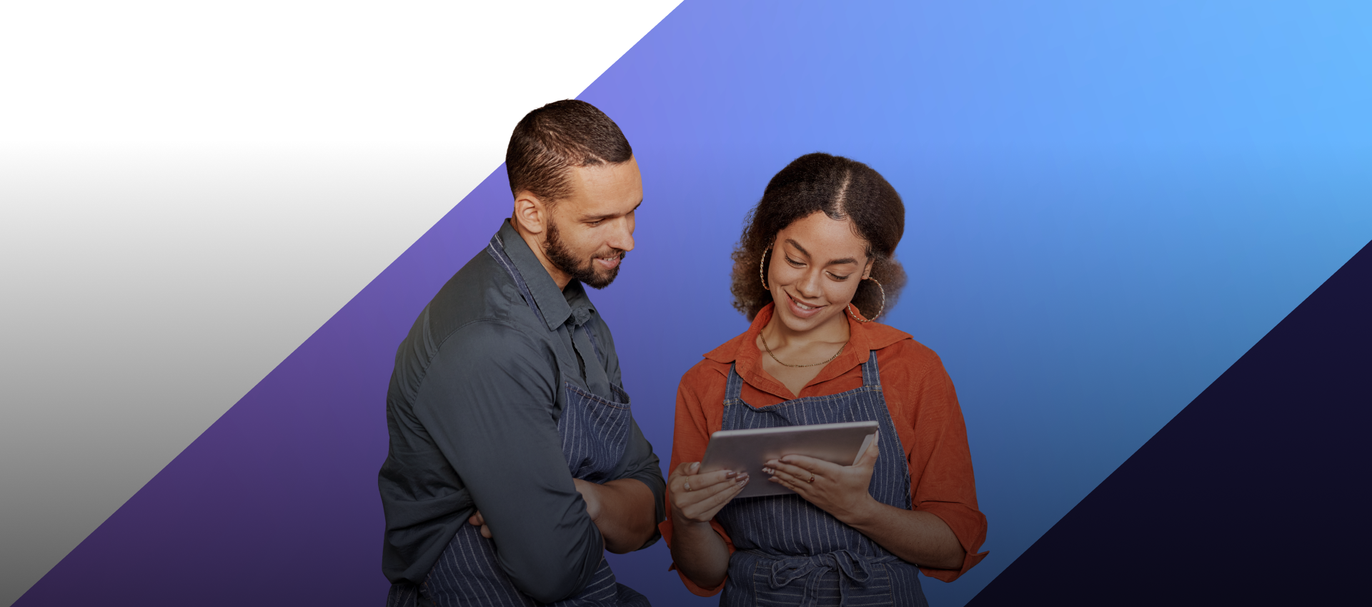 Two business owners, a man and a woman, wearing aprons, look at a tablet together.