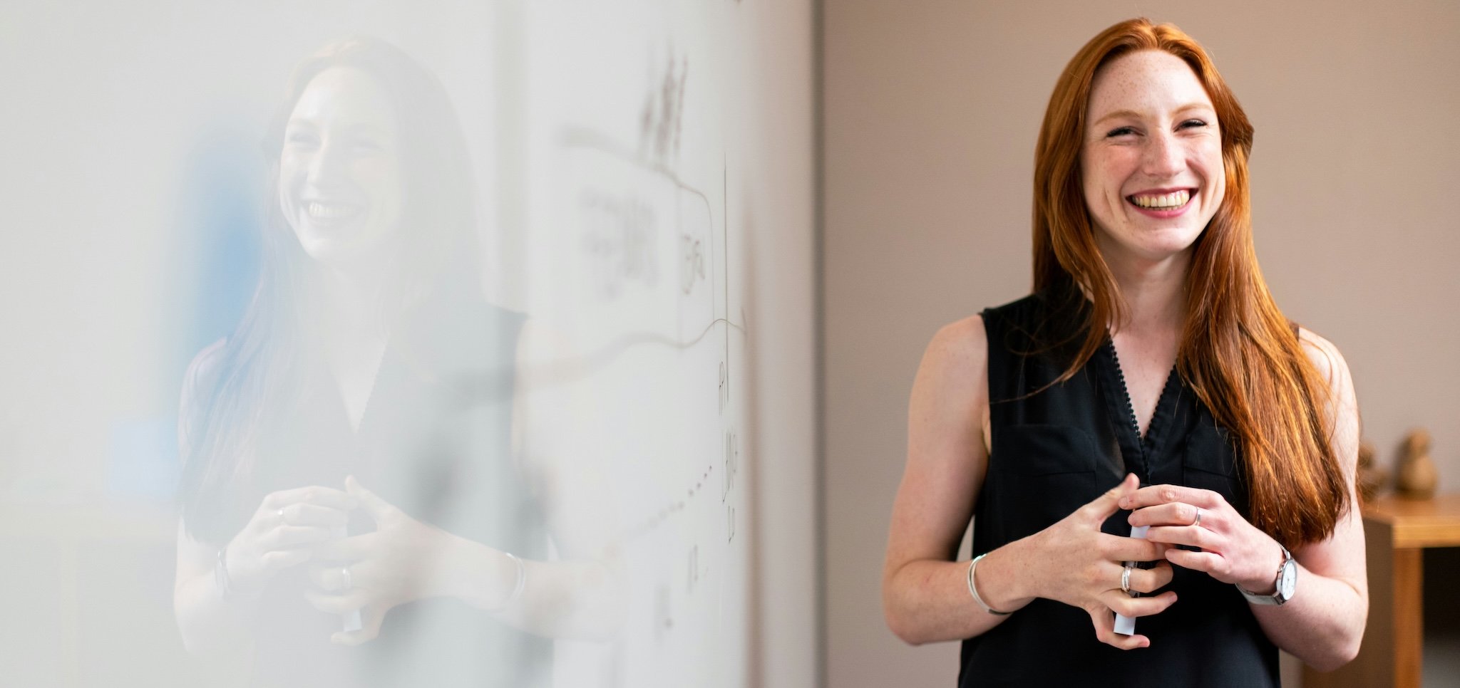 A smiling woman with red hair standing next to a whiteboard with sketches on it.