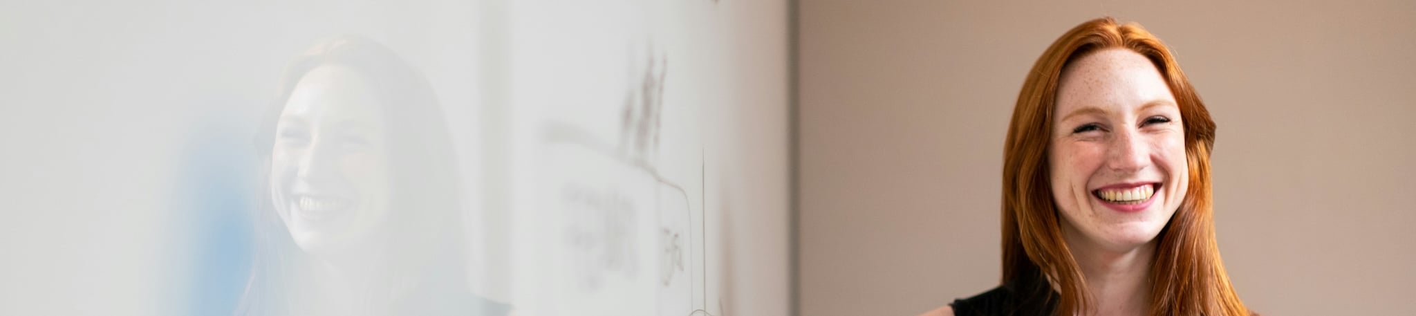 A smiling woman with red hair standing next to a whiteboard with sketches on it.