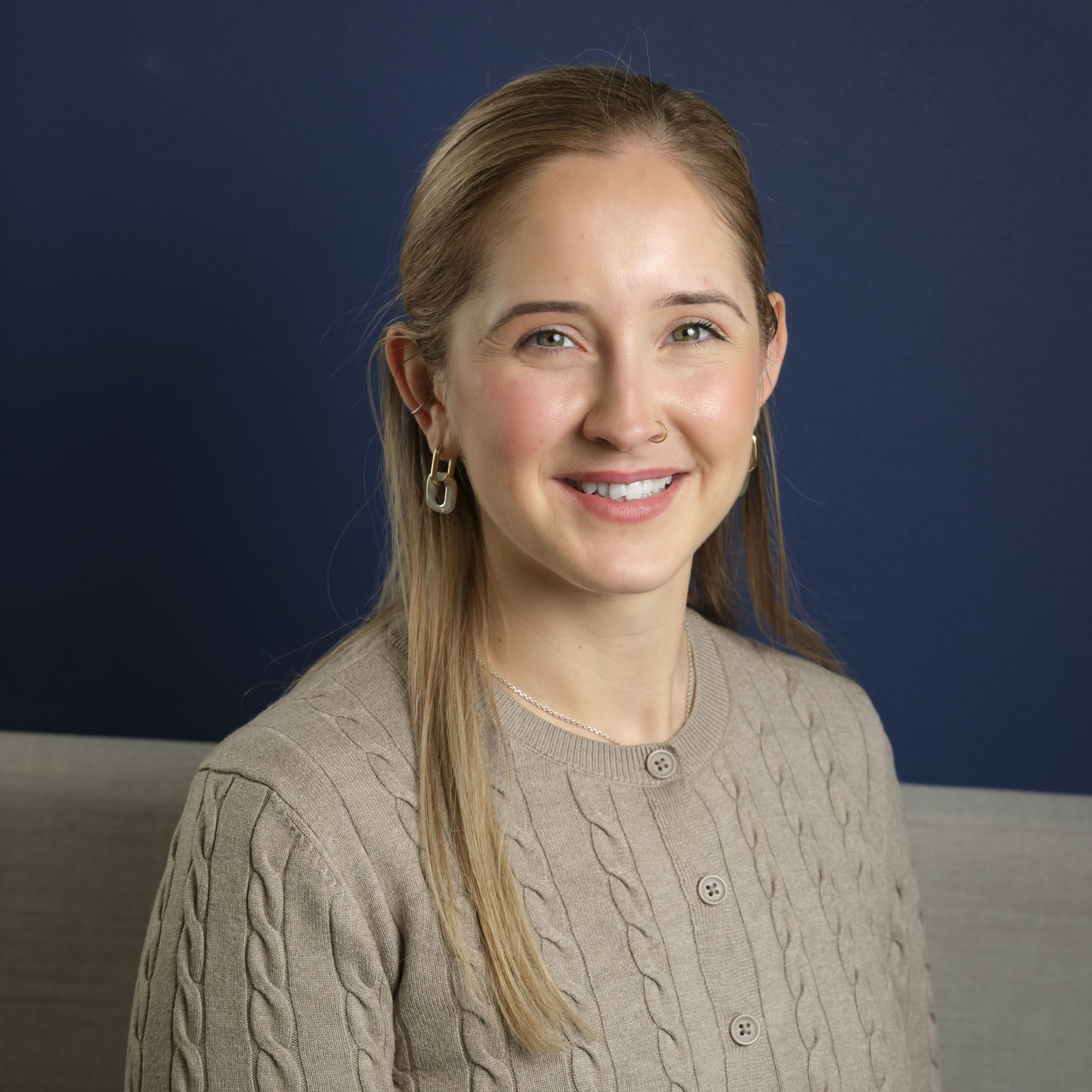 Dixie Madden smiling in a beige cable-knit sweater against a dark blue background.