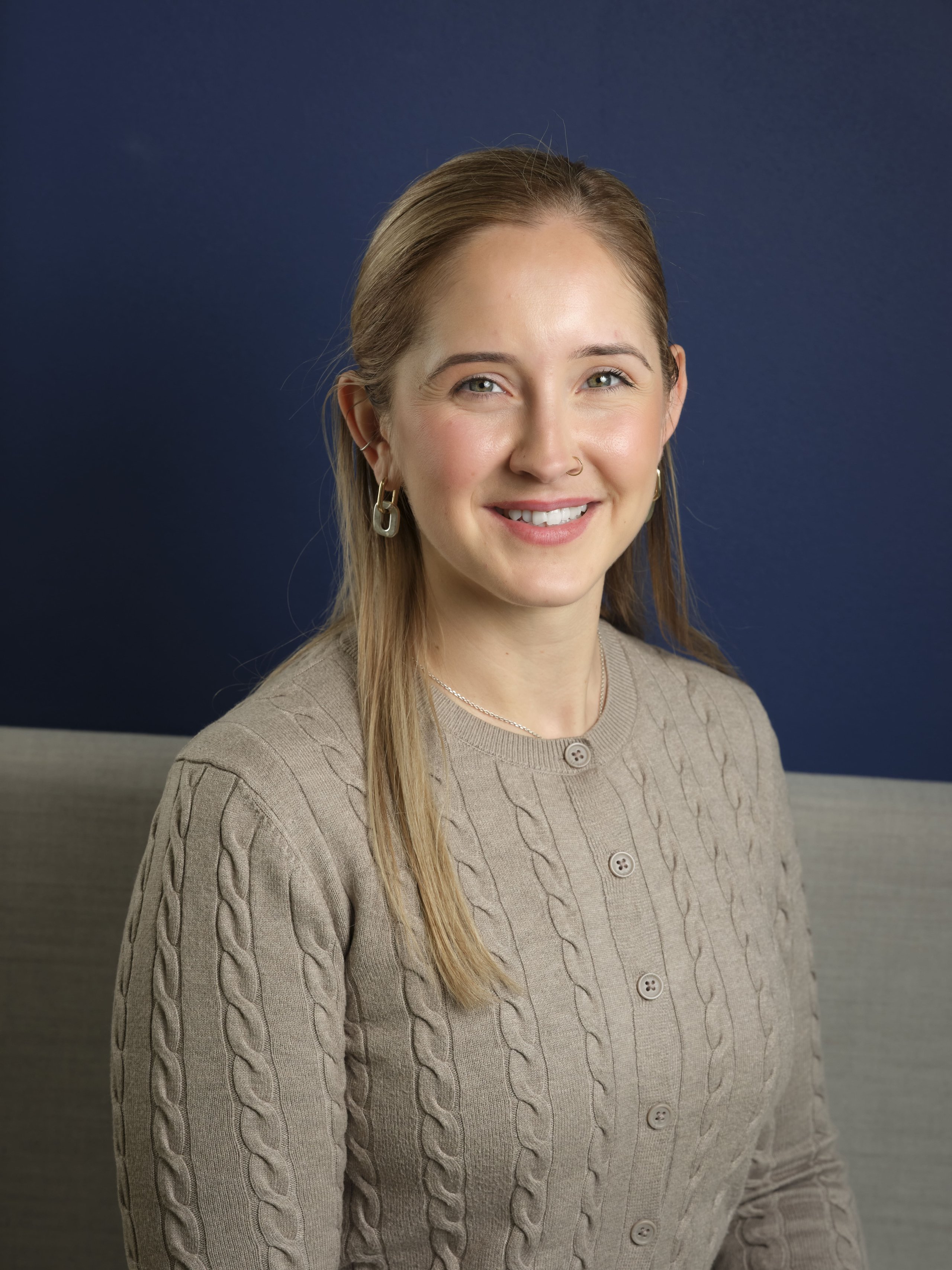 Dixie Madden smiling in a beige cable-knit sweater against a dark blue background.